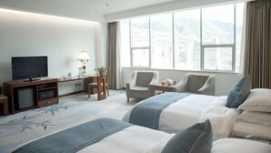 A hotel room with two beds, a TV, a desk with a lamp, and a view of mountains through large windows. - Nujiang Hotel (Lushui)