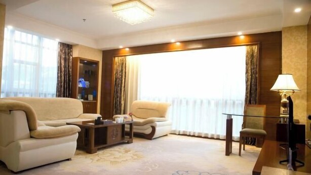 Un salón amplio con sofá, sillón y una mesita. Cuenta con un ventanal con cortinas, una lámpara y un televisor.