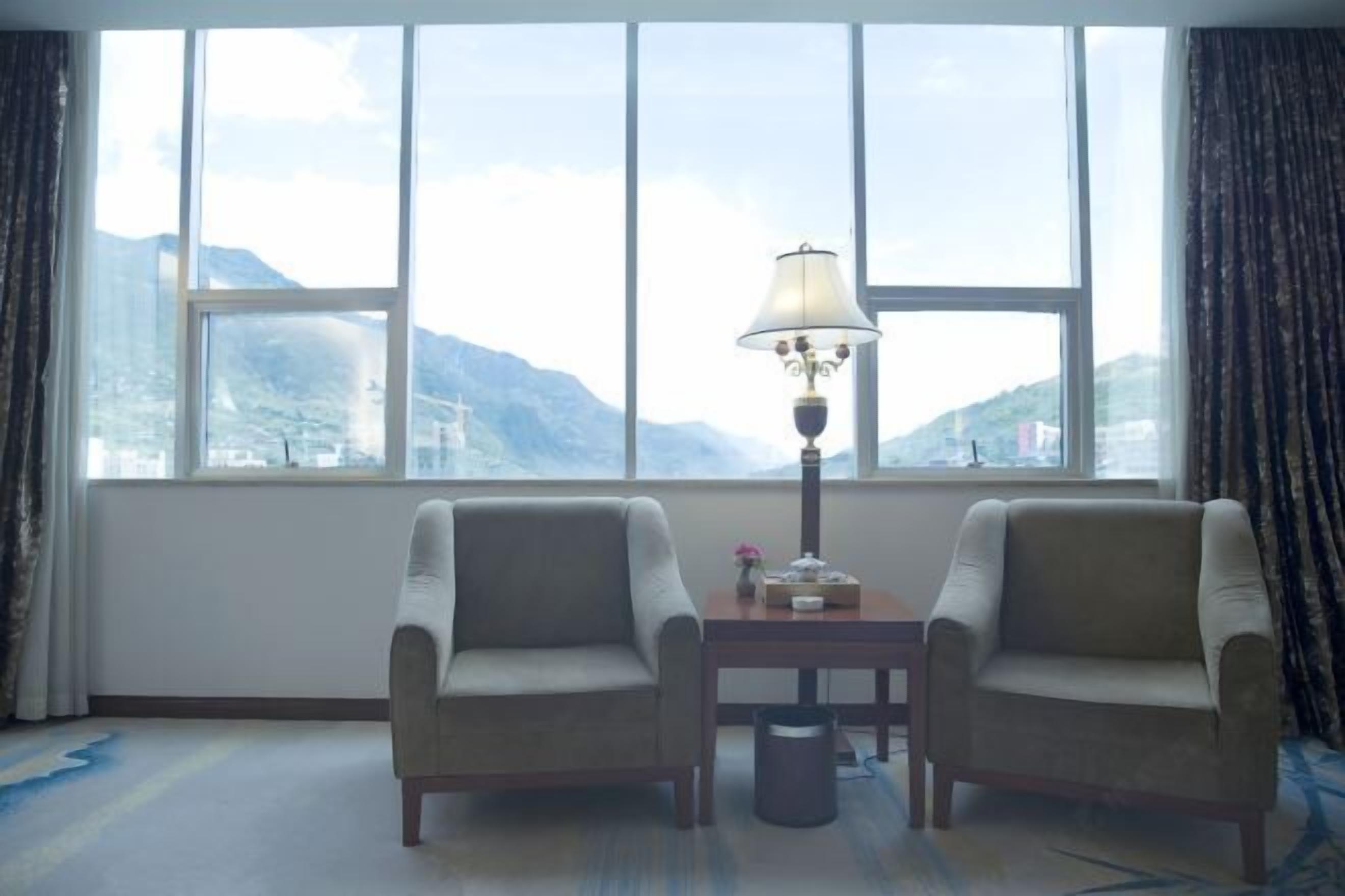 A room with two armchairs, a table, a lamp, and a view of mountains through large windows.