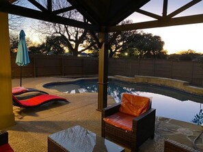 Uma área externa coberta com piscina, espreguiçadeiras e uma mesa.