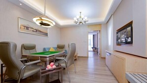 Un salon moderne doté d’une table de billard, de sièges confortables, d’un lustre et d’un téléviseur fixé au mur.