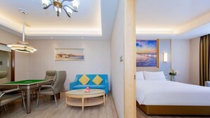 Une chambre d’hôtel avec un lit, une table de billard, un canapé bleu et un tableau représentant un coucher de soleil.