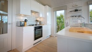 Une cuisine moderne avec des meubles blancs, un îlot central et une vue sur la verdure à l’extérieur.