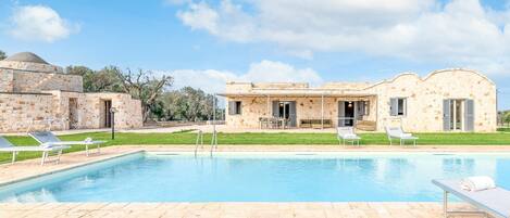 A pool area with lounge chairs and a building with stone walls and a dome structure.