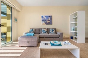 A modern living room with a grey sofa, a white coffee table, and a painting of a coastal scene. - Ocean View / 1 bedroom condo with Infinity pool (Isla Mujeres)