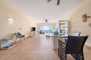 A spacious living area with a glass dining table, a ceiling fan, and a view of the ocean. - Ocean View / 1 bedroom condo with Infinity pool (Isla Mujeres)