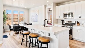 A modern kitchen with white cabinets, a large island with stools, a microwave, stove, and a sink. - Paseos Poolhouse by RedAwning (Washington)