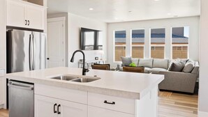 A modern kitchen with white cabinetry, a stainless steel refrigerator, and a large island with a sink. - Paseos Poolhouse by RedAwning (Washington)