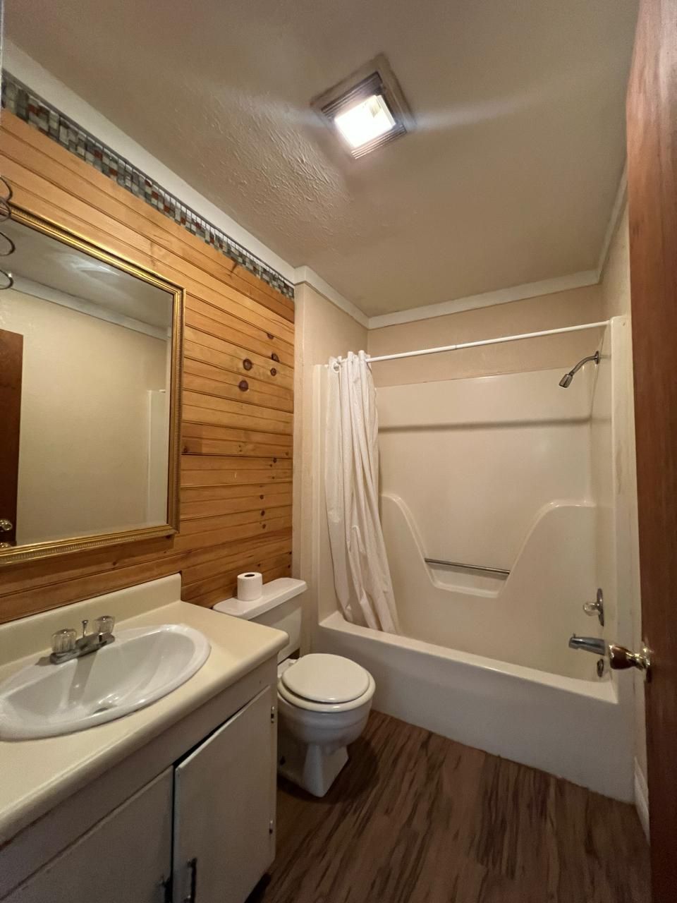 Un baño con pared de paneles de madera, un lavabo blanco, un inodoro y una bañera.