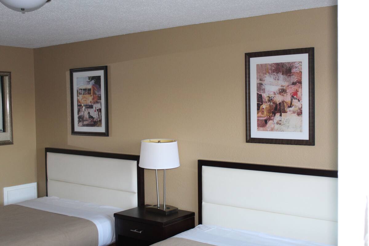 A hotel room with two beds, a nightstand with a lamp, and two framed pictures on the wall.