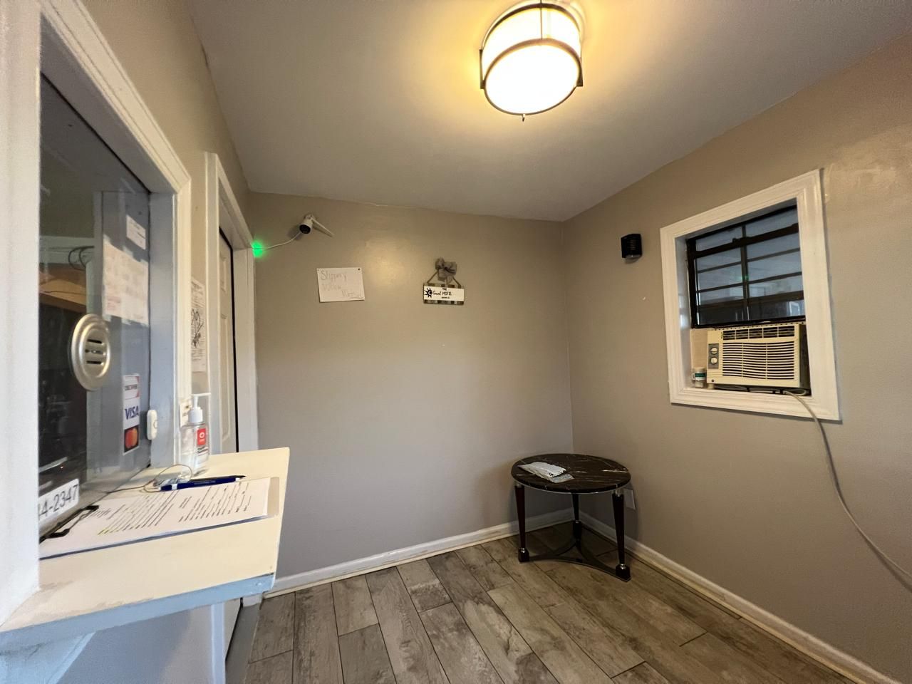 A room with a wooden floor, a small round table, a window with an air conditioner, and a door with a glass panel.