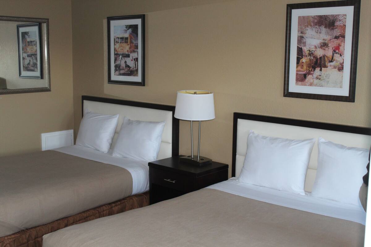 A hotel room with two beds, a nightstand with a lamp, and framed pictures on the wall.