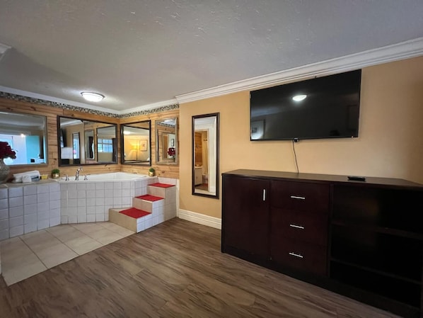 A bathroom with a bathtub, a sink, and a mirror. There is a staircase leading to another room.