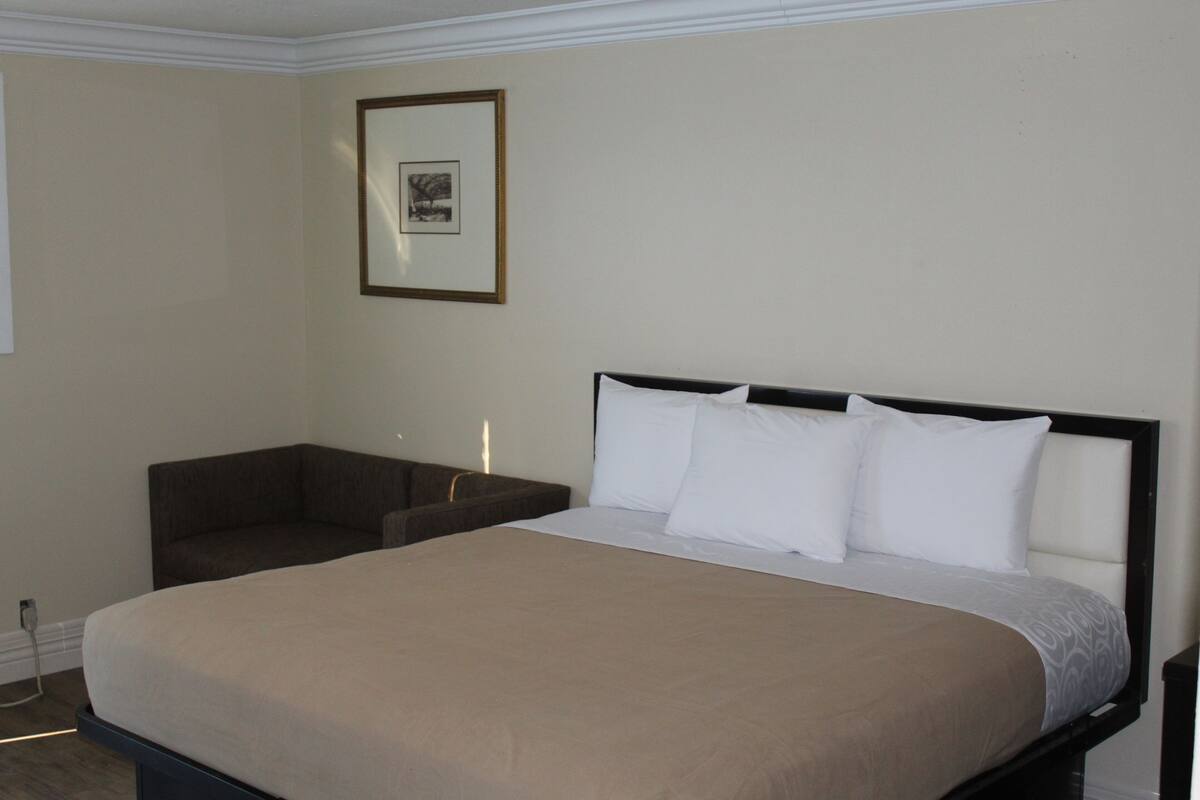 A hotel room with a bed, a nightstand, a framed picture on the wall, and a window.