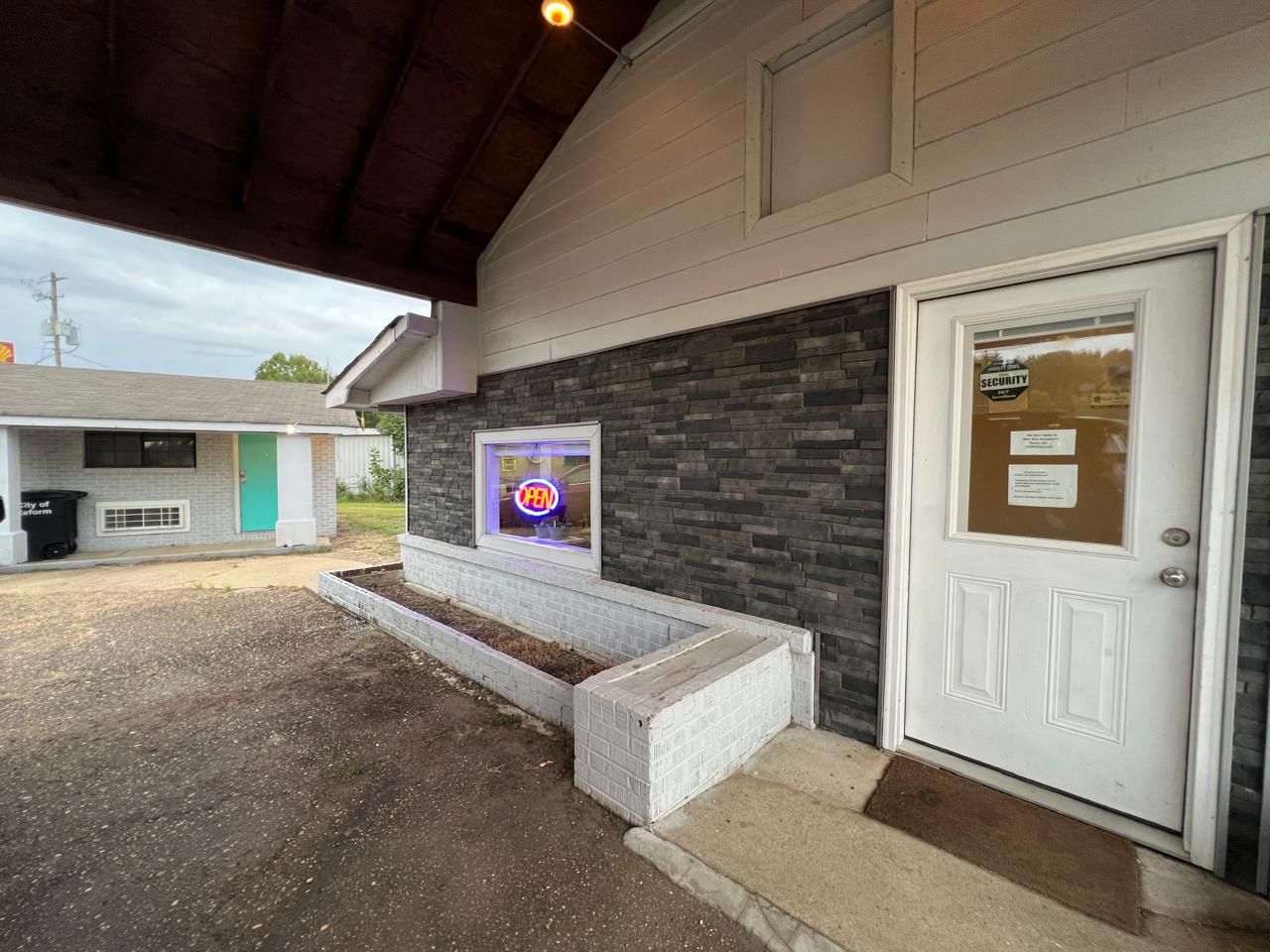 A building with a white door, a security notice, and a neon sign.
