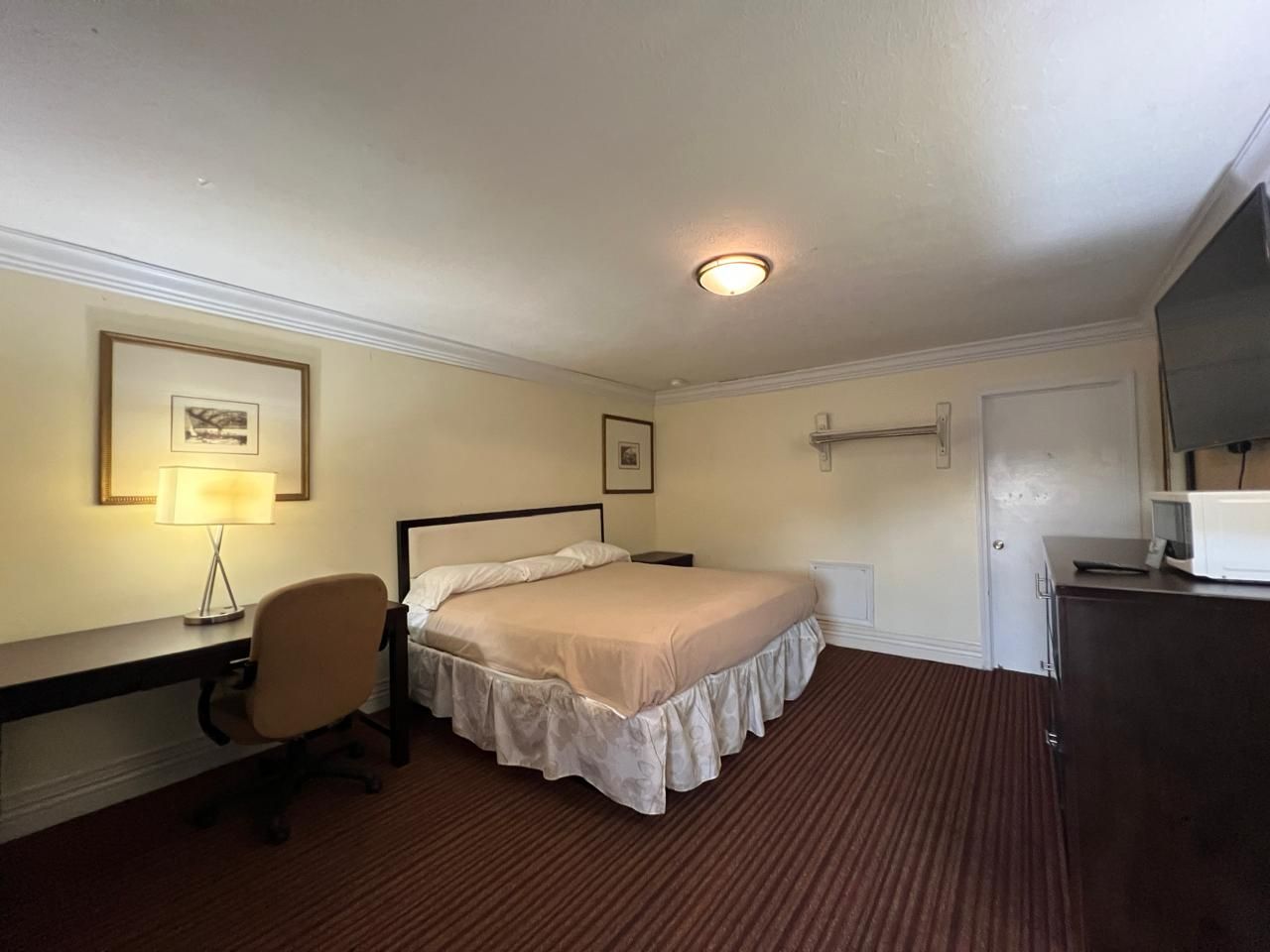 A hotel room with a bed, desk, chair, and a television.