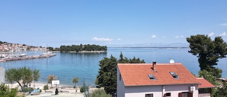 Une vue sur la côte, avec un port de plaisance, un bâtiment blanc doté d’un toit rouge et un ciel bleu dégagé.