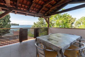 Eine Terrasse im Freien mit Tisch und Stühlen, mit Blick auf ein Gewässer und Bäume.