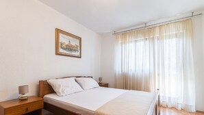 Ein Schlafzimmer mit Bett, Nachttischen, einer Lampe, einem gerahmten Bild und transparenten Vorhängen.