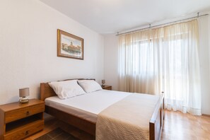 A bedroom with a bed, nightstands, a lamp, a framed picture, and sheer curtains.
