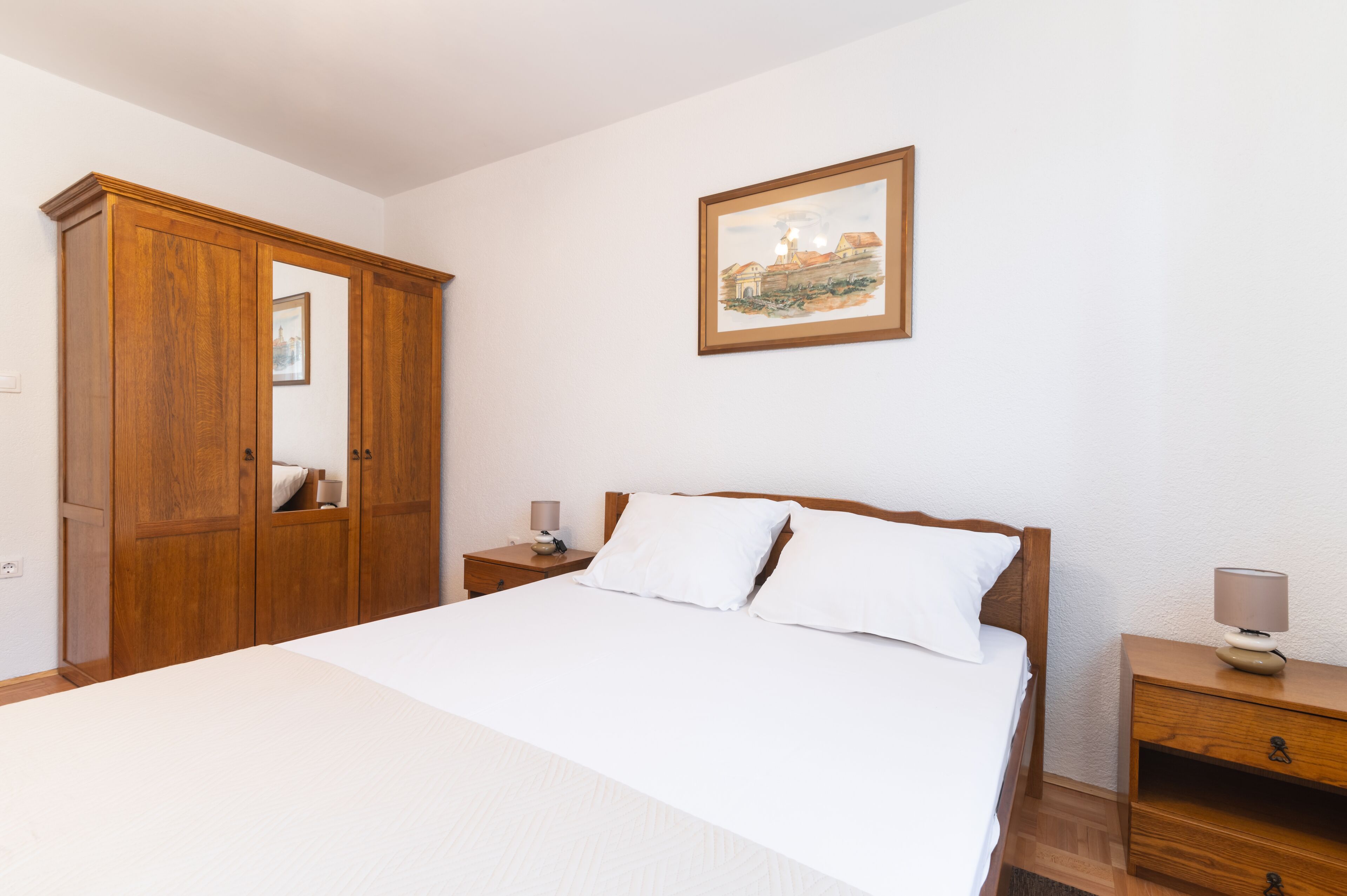 A bedroom with a bed, wooden wardrobe, bedside tables, and a framed picture on the wall.