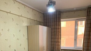 Une chambre à coucher avec un lit, une armoire, un radiateur et une fenêtre avec des rideaux.