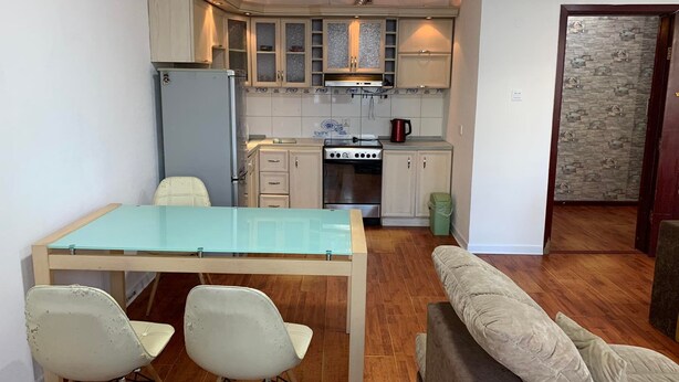 Une cuisine compacte avec une table en verre et deux chaises, un canapé et un mur décoré d’un motif imitant la pierre.