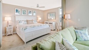 Un dormitorio con cama, mesitas de noche, cómoda y un sofá verde, además de obras de arte en las paredes.