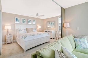 Quarto com cama, mesas de cabeceira, cômoda, sofá verde e obras de arte nas paredes.
