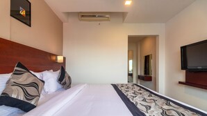 A hotel room with a large bed, a flat-screen TV, a wooden headboard, and a wall-mounted air conditioner.