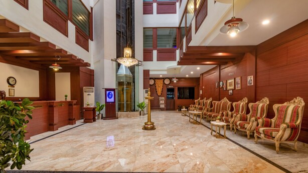 A lobby with a marble floor, wooden reception desk, and rows of ornate chairs.