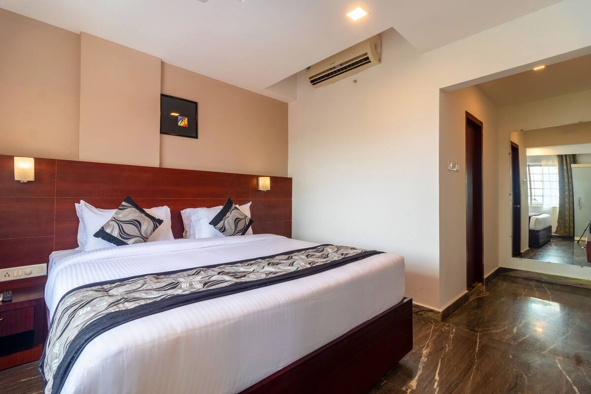 Una habitación de hotel con una cama grande, un cabecero de madera, aire acondicionado instalado en la pared y una mesita de noche pequeña.