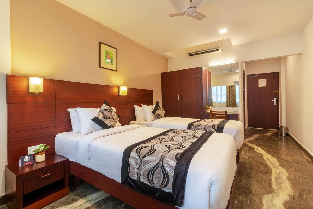 Habitación de hotel con dos camas, cabeceros de madera, lámparas de noche, ventilador de techo y un espejo grande.