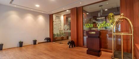 A spacious lobby with wooden flooring, a reception desk, a large mirror, and a decorative elephant statue.