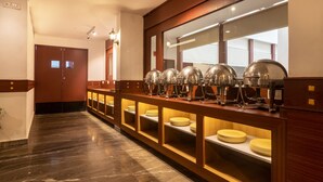 A hotel corridor with a buffet setup featuring multiple serving stations with food covers and stacked plates.