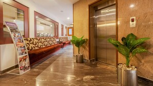 A hotel lobby with a marble floor, a reception desk, a sofa, an elevator, and potted plants.