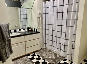 Une salle de bain avec un carrelage noir et blanc à motifs de damier, un lavabo blanc avec un miroir au-dessus, une serviette accrochée au mur et un rideau de douche à motifs de quadrillage noir.
