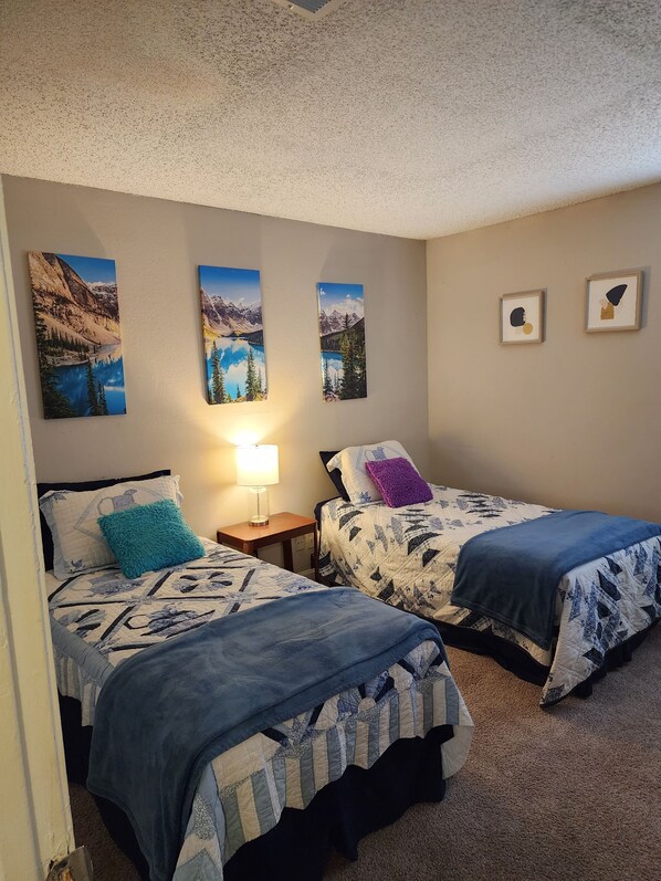 A bedroom with two beds, a nightstand, a lamp, and three framed pictures on the wall.