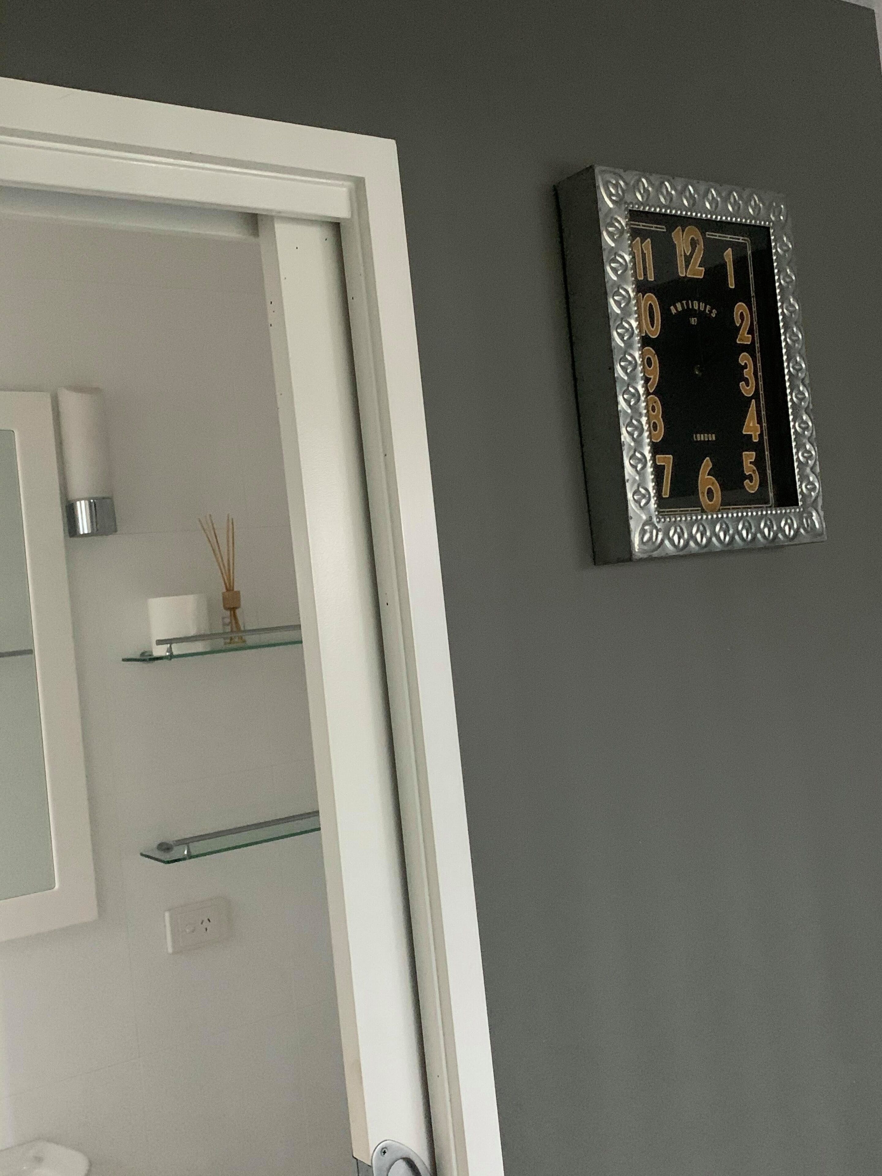 A bathroom with a white door, a wall-mounted clock, and a mirror.