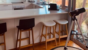 A modern kitchen with white cabinets, a countertop, and a large window overlooking a scenic landscape. - Immaculate designer house-sweeping views over iconic Blueys Beach 3min walk away (Blueys Beach)
