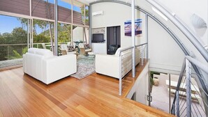 A modern interior with a curved ceiling, a seating area with a sofa and chairs, a flat-screen TV, and a kitchen area. - Immaculate designer house-sweeping views over iconic Blueys Beach 3min walk away (Blueys Beach)