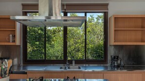 A modern kitchen with a central island, stainless steel appliances, and a window with a view of greenery. - Villa Balangan Sunset (Jimbaran)