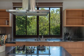 A modern kitchen with a central island, stainless steel appliances, and a window with a view of greenery.