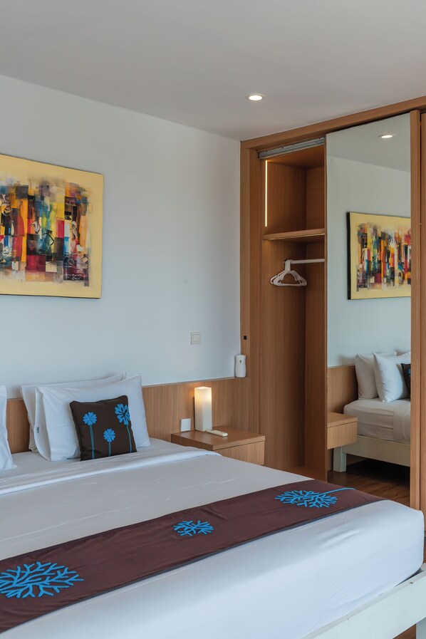 A hotel room with a bed, a bedside table with a lamp, a wooden wardrobe, and two abstract paintings on the walls.