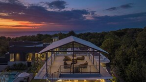 A modern house with a glass-enclosed patio area, a swimming pool, and a view of the ocean at sunset. - Villa Balangan Sunset (Jimbaran)