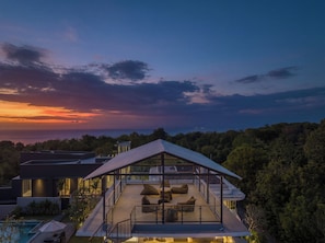 Une maison moderne dotée d’un patio entièrement vitré, d’une piscine et offrant une vue sur l’océan au coucher du soleil.