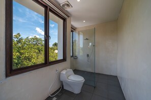 A modern bathroom with a toilet, a glass shower enclosure, and a window with a view of trees.