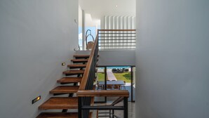 A modern staircase with wooden steps and metal railings, leading to a balcony with a view of a garden and a parked car. - Villa Balangan Sunset (Jimbaran)