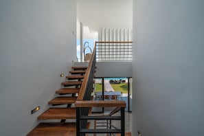 A modern staircase with wooden steps and metal railings, leading to a balcony with a view of a garden and a parked car.