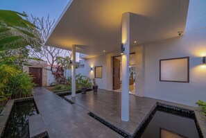 A modern building with a covered outdoor area, potted plants, and a water feature.